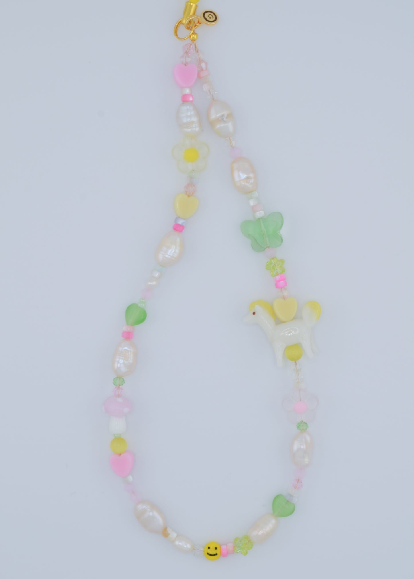 A closer view of the phone charm showcasing the soft pastel colors of the shell beads and freshwater pearls. The charm also features a small, delicate pony lampwork bead, surrounded by flower and heart-shaped glass beads, making it a charming accessory.
