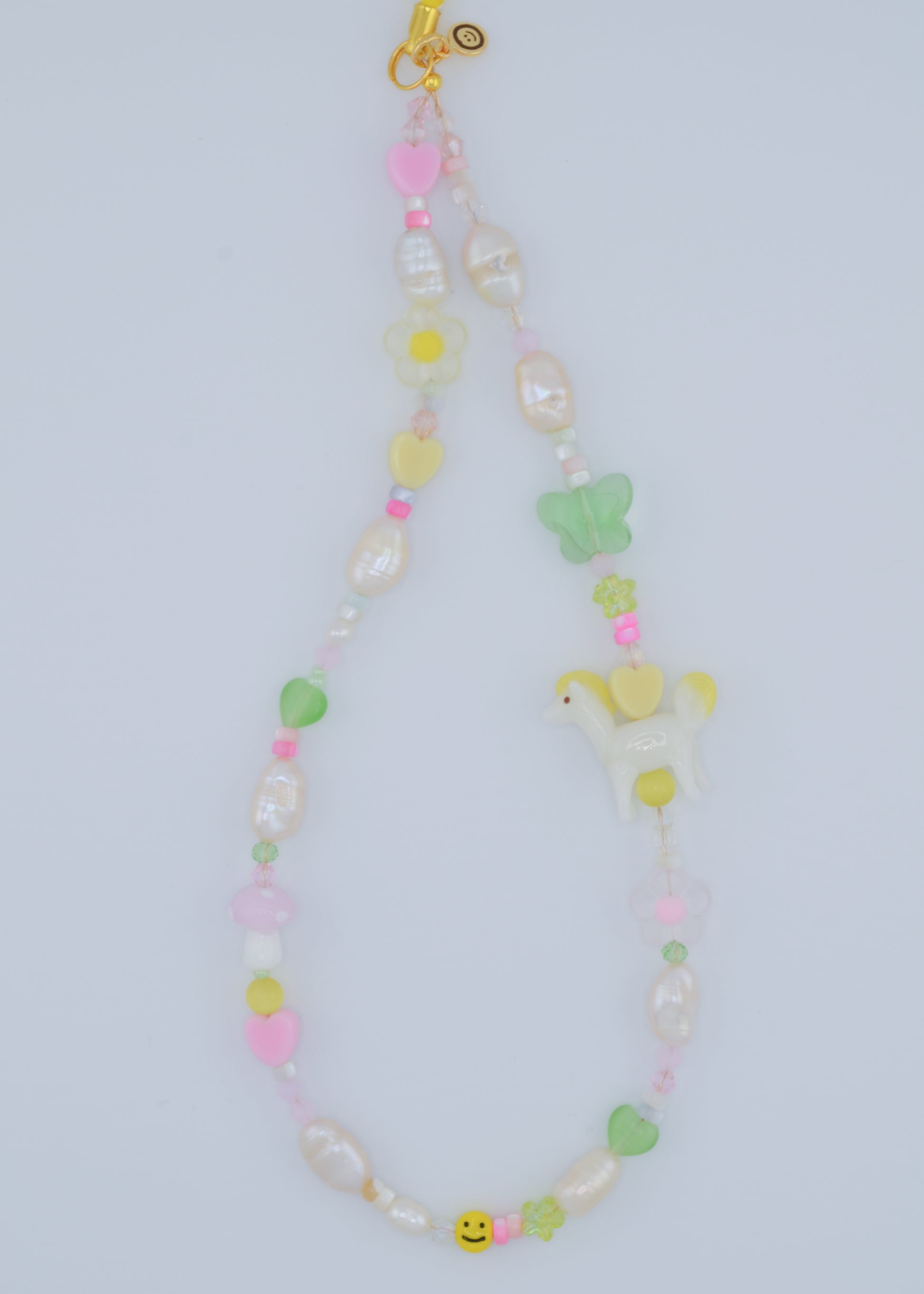 A closer view of the phone charm showcasing the soft pastel colors of the shell beads and freshwater pearls. The charm also features a small, delicate pony lampwork bead, surrounded by flower and heart-shaped glass beads, making it a charming accessory.
