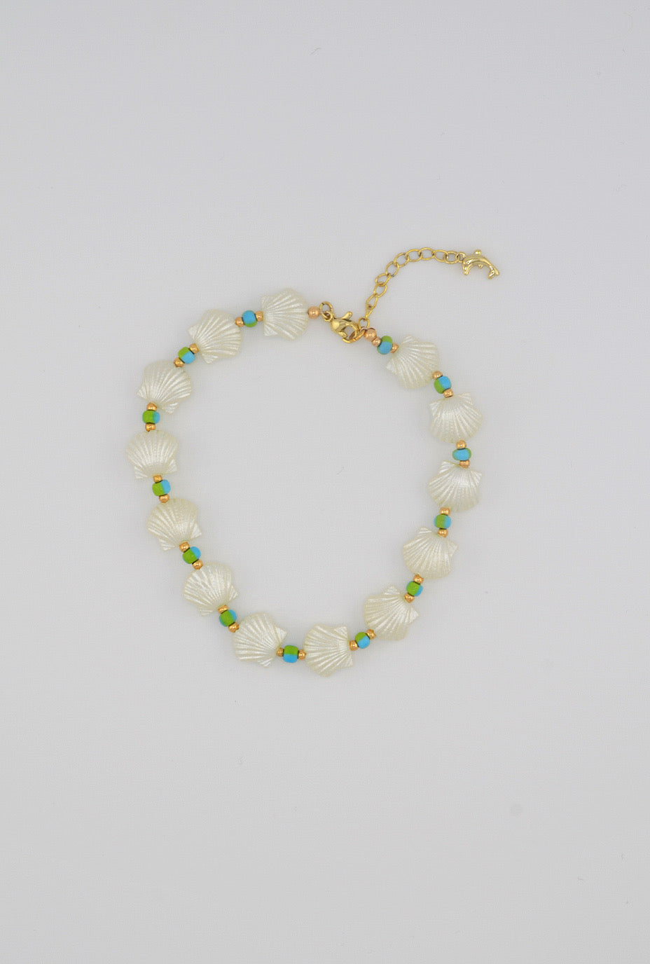 A minimalist anklet with glossy white seashell beads complemented by turquoise seed beads and golden spacers, and adorned with a small dolphin-shaped clasp for an ocean-inspired look.