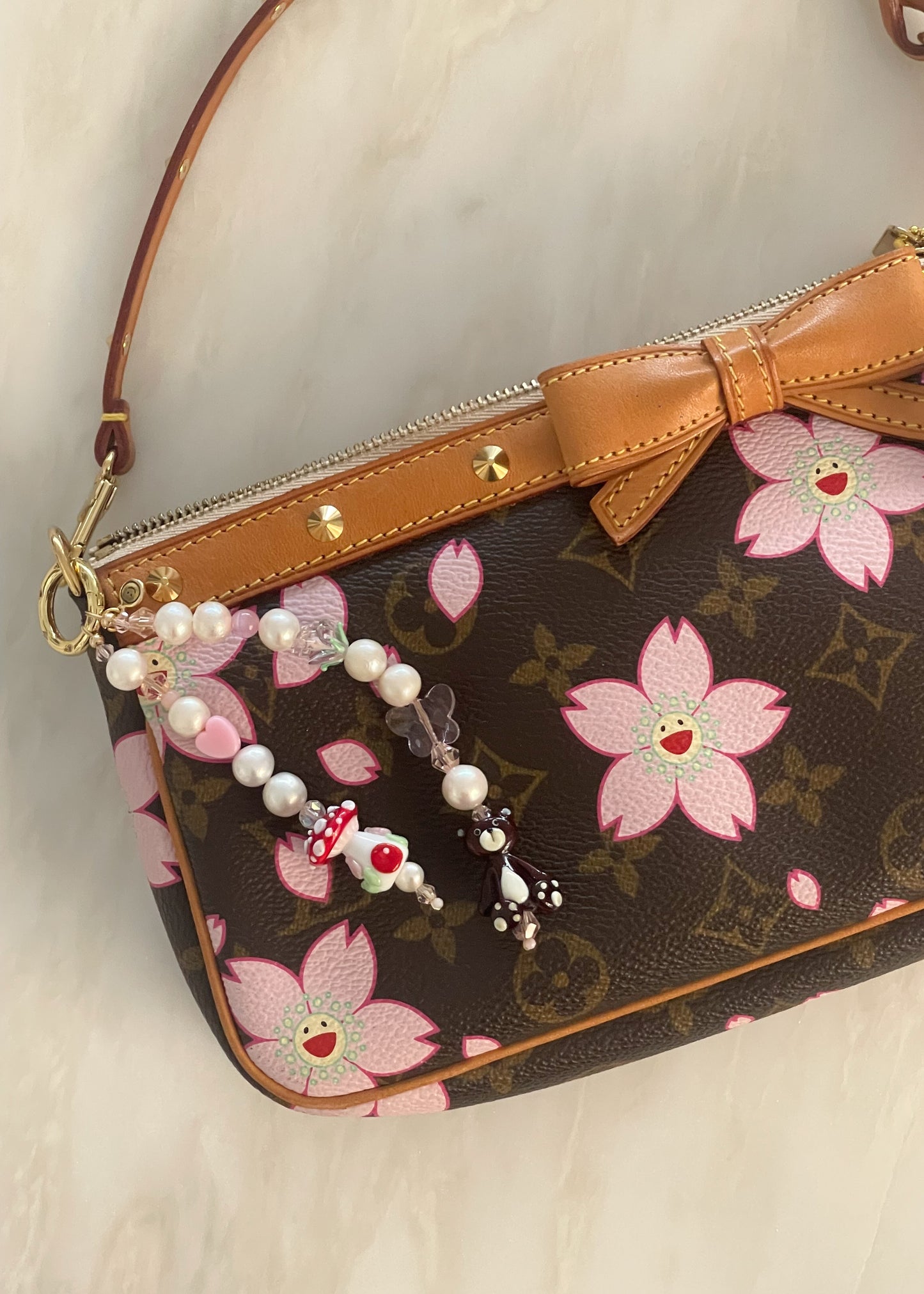 The bag charm attached to a designer purse with a pink cherry blossom pattern and brown leather trim. The charm’s playful beads and pearls contrast beautifully with the elegant bag design.
