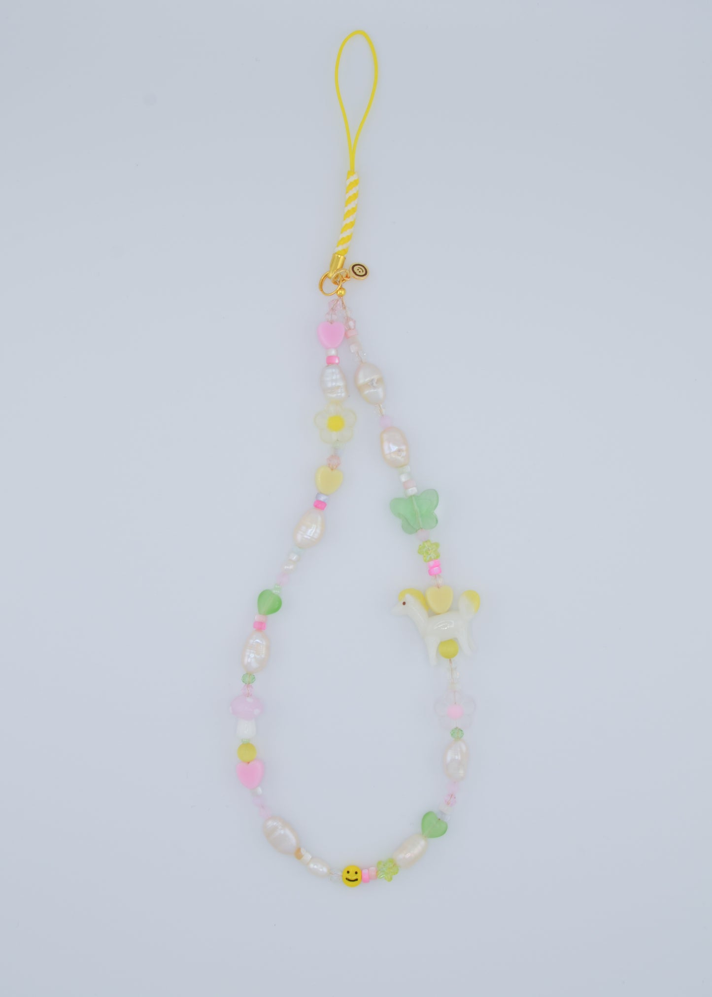 A vibrant phone charm made with a mix of shell beads, freshwater pearls, and whimsical lampwork glass beads. The design features a playful combination of pastel hearts, flowers, and a small white pony, creating a fun and cheerful accessory for your phone.