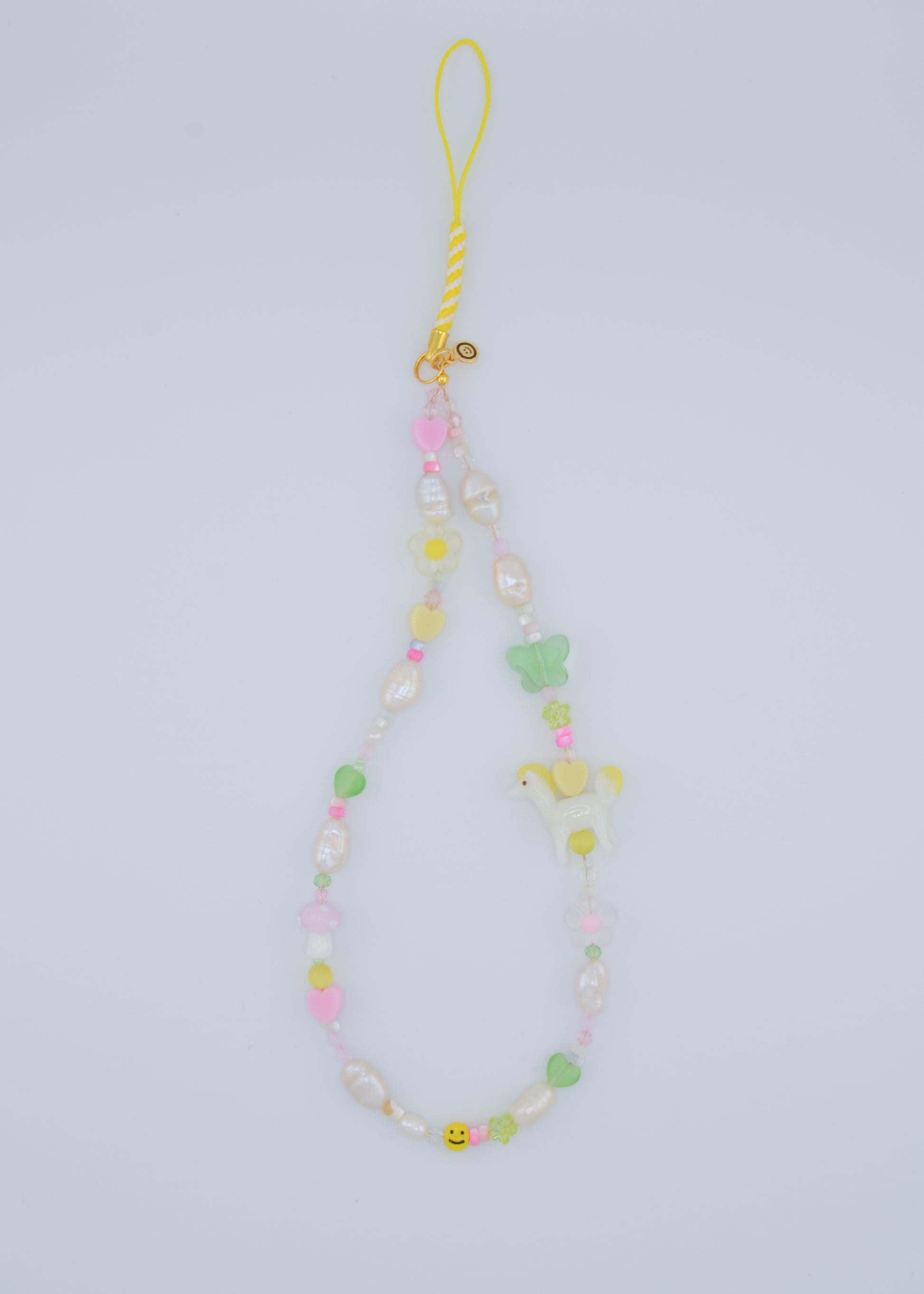 A vibrant phone charm made with a mix of shell beads, freshwater pearls, and whimsical lampwork glass beads. The design features a playful combination of pastel hearts, flowers, and a small white pony, creating a fun and cheerful accessory for your phone.