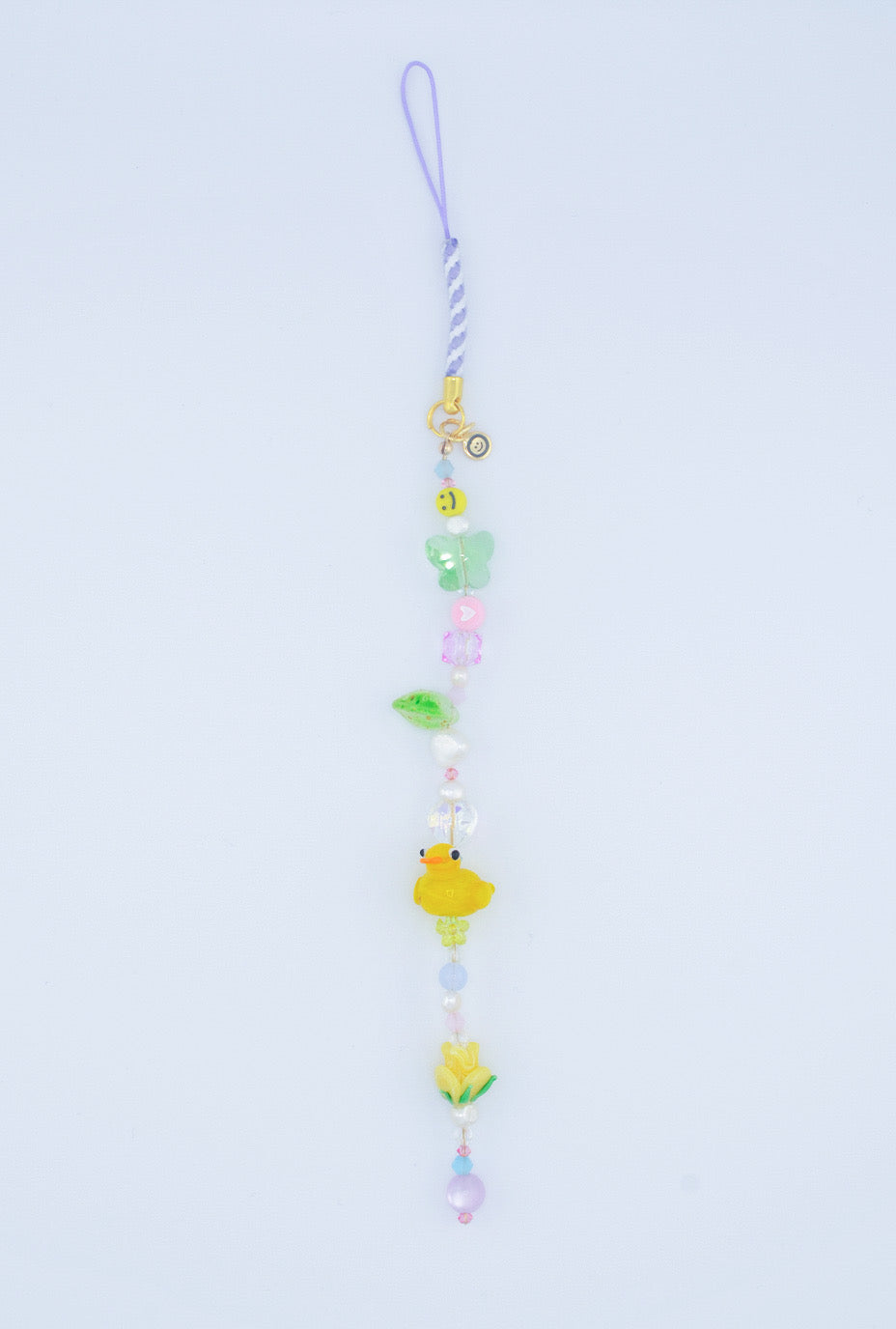A colorful phone charm with smiley faces, butterfly and flower glass beads, green hearts, a yellow duck lampwork bead. It also features vibrant details in the form of candies and playful beads.