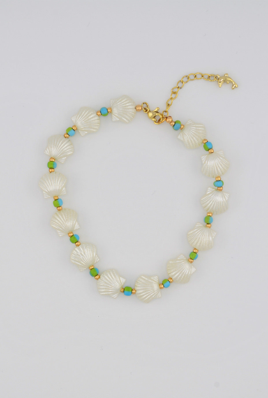 A delicate anklet featuring lustrous white seashell beads interspersed with turquoise and golden seed beads, finished with a small dolphin charm for a beachy, summery vibe.