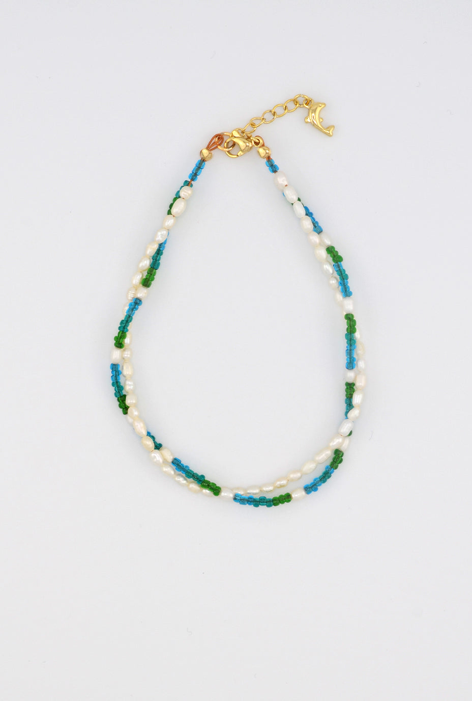 A delicate handmade anklet featuring a combination of freshwater pearls and multicolored glass beads in shades of green and blue, with a gold-tone clasp adorned with a dolphin charm for a playful ocean-inspired touch.