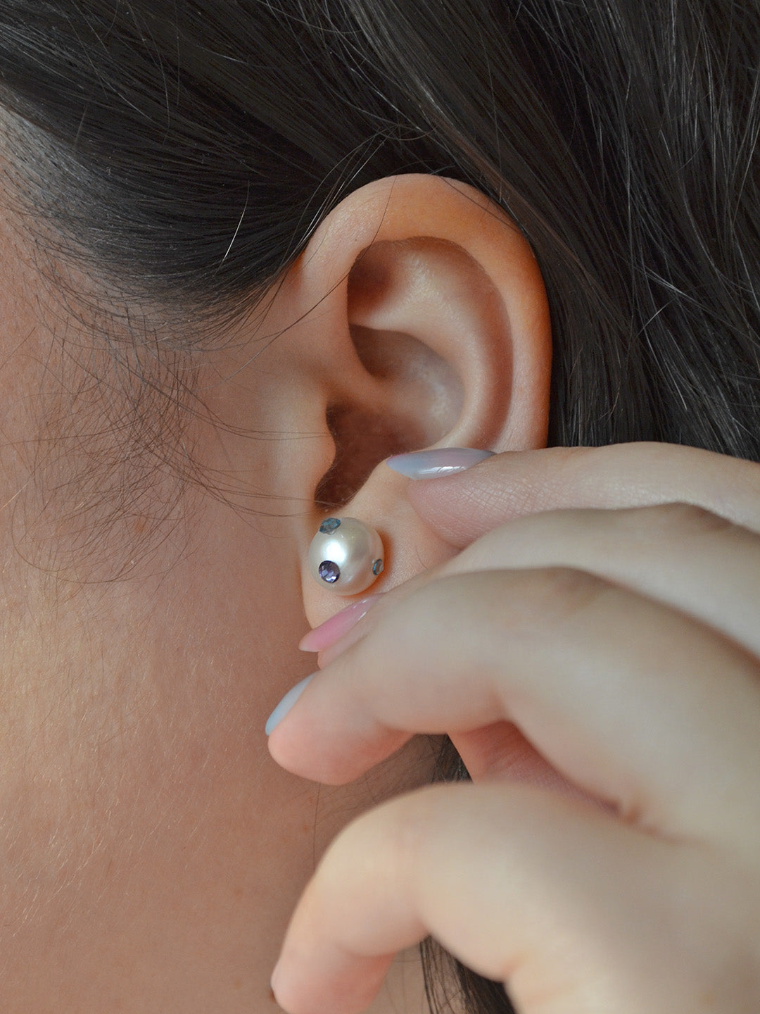Pearl earring with a fun and unique design, featuring blue and purple crystal gemstones on the ear of the wearer. The earrings add a touch of elegance with a playful cute twist.