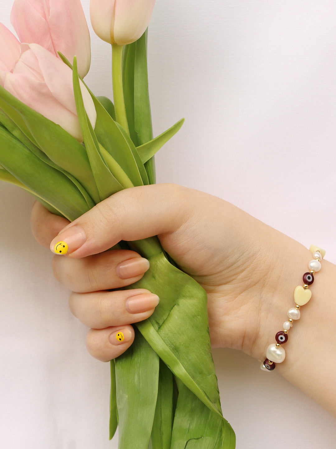 Worn on the wrist, this bracelet adds a cheerful touch with its yellow and burgundy beads, paired elegantly with soft tulips.