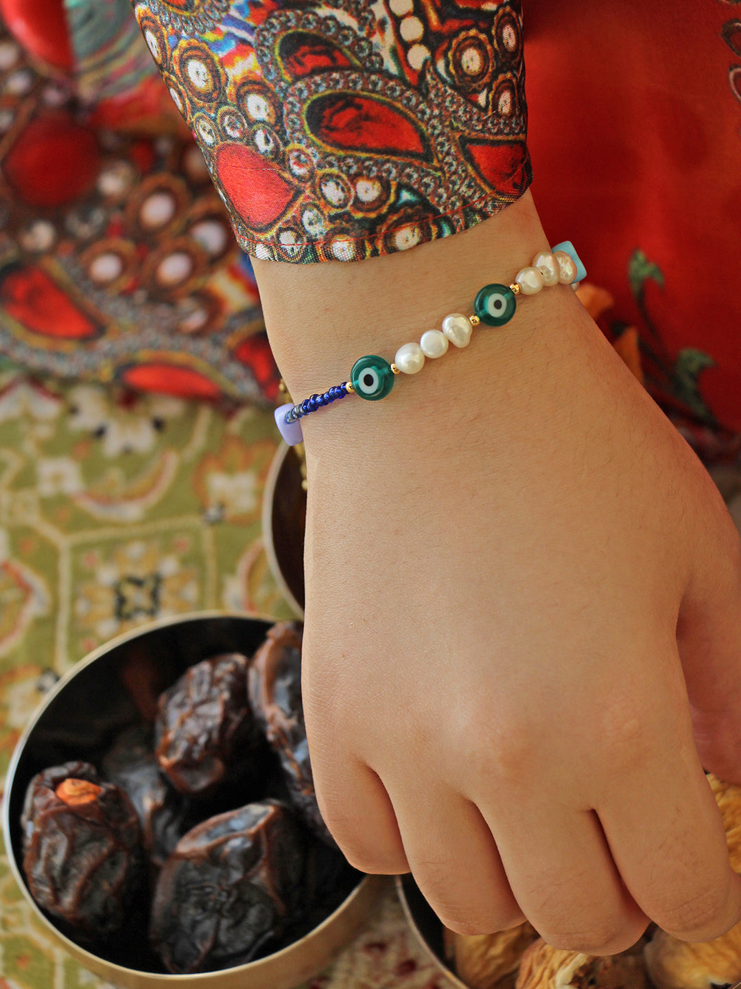 Styled on the wrist, this bracelet’s pearls and charms pop against vibrant fabric, blending elegance with cultural charm.