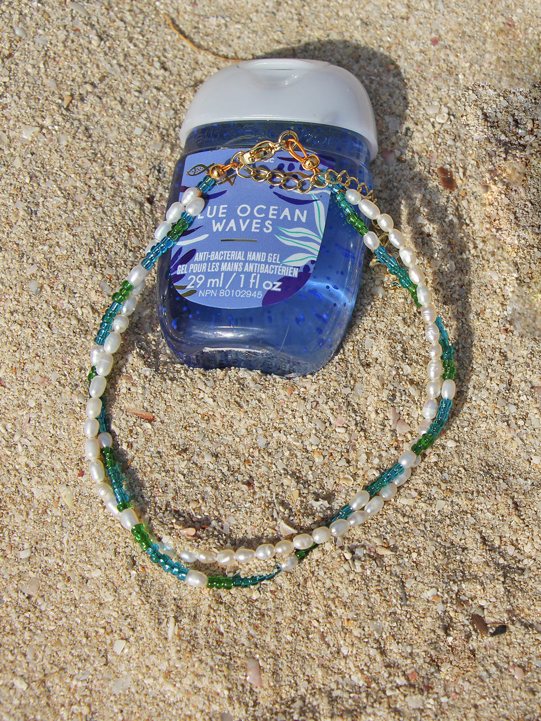 This anklet combines serene ocean blues and greens with smooth freshwater pearls, perfect for a beachy vibe, accompanied by a gold-tone dolphin charm and a gold clasp.